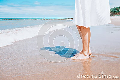 Barefoot woman wearing white skirt posing touching water with her feet. Summer, vacation. Copyspace Stock Photo