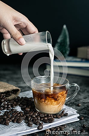 Barista making latte. hand pouring milk into a cup of espresso coffee, preparing coffee drink. vertical image, cropped shot. Stock Photo