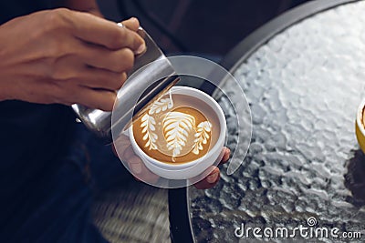 Barista pouring milk foam for making coffee latte art with pattern the leaves in a cup Stock Photo
