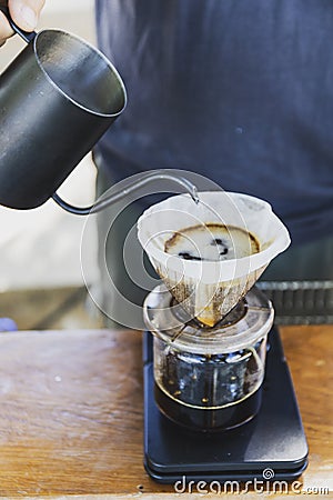 Barista spills hot water prepare filtered coffee from stainless steel teapot to drip paper maker on black simple weights. Stock Photo