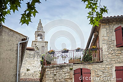 Barjac, France. Bell tower, building facade with wooden shutters and terrace with flowers. View of old european town village Stock Photo