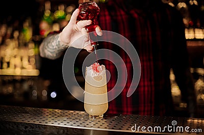 Barman adding sweet red liqueur into a glass with fresh sweet juicy cocktail Stock Photo