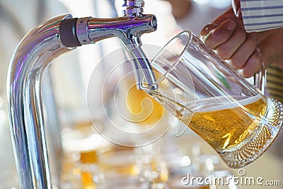 Barman pours a light foamy beer into a large mug during the Oktoberfest party. Stock Photo