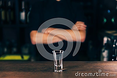 Barmen hand with bottle pouring beverage into glass. Bartender pouring strong alcoholic drink into small glass on bar Stock Photo