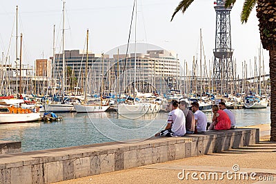 BARSELONA, SPAIN - AUGUST 6, 2019: A group of people sit in the shade and look at yachts in the port of Barcelona Editorial Stock Photo