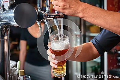 Bartender pouring beer from tap behind bar. Blurred woman in the background Stock Photo