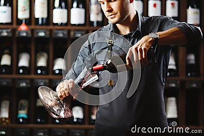 Bartender pours red wine in transparent vessel in cellar Stock Photo