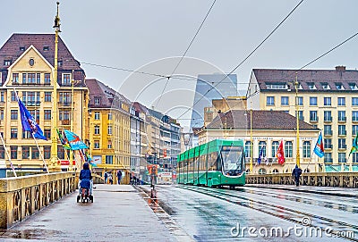 The view on modern green tram ridding on Mittlere Brucke on rainy day in Basel, Switzerland Editorial Stock Photo