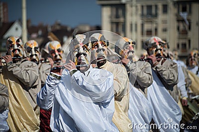 Masked people wearing traditional costume playing flute parading in the street Editorial Stock Photo