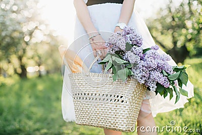 Basket with bouquet of lilacs and baguette in woman hands on background of nature Stock Photo