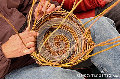 Basket maker weaves wood strands in circular basket. Stock Photo