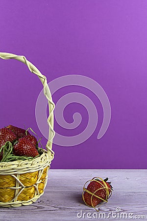 Basket with strawberries is on the table. One berry lies nearby. Purple background. Stock Photo