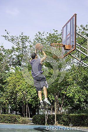 Basketball in hand man jumping Throw a basketball hoop Background tree in park Stock Photo