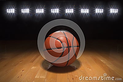 Basketball on wood floor beneath bright lights Stock Photo