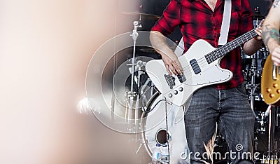 Bass guitarist in a rock or heavy metal band in a red and black plaid flannel shirt playing bass guitar on stage at a festival Stock Photo