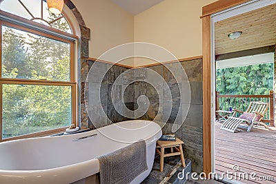 Bathroom interior with grey tiles and free standing white tub with open door to the balcony and oval window Stock Photo
