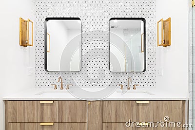 A bathroom with a wood cabinet, gold sconces, and tiled backsplash. Stock Photo