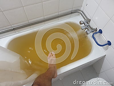 bathtub full of yellow water due to rust or impurities with human leg entering. Stock Photo