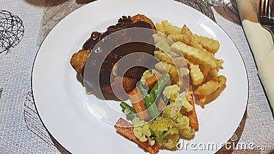 Battered chicken, fried potatoes and boiled cauliflower and carrots on a white plate. Stock Photo