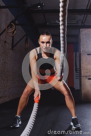 Fit sportswoman working out in gym doing cross fit exercise with ropes Stock Photo