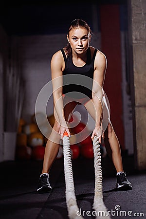 Fit sportswoman working out in gym doing cross fit exercise with ropes Stock Photo