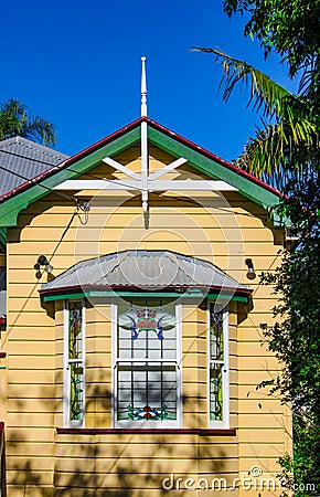 Bay window on yellow traditional Australian Queenslander House with tin roof and tropical trees Stock Photo