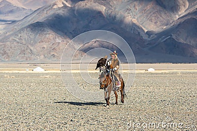 Kazakh Eagle Hunter at traditional clothing, on horseback while hunting to the hare holding a golden eagle on his arm in desert mo Editorial Stock Photo