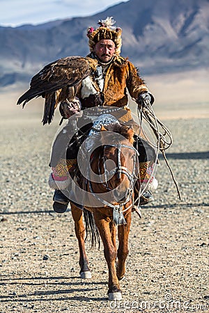 Kazakh Eagle Hunter at traditional clothing, on horseback while hunting to the hare holding a golden eagle on his arm Editorial Stock Photo