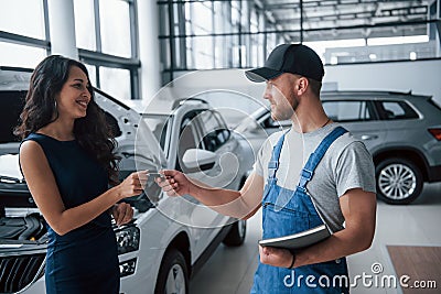 Be careful next time. Woman in the auto salon with employee in blue uniform taking her repaired car back Stock Photo