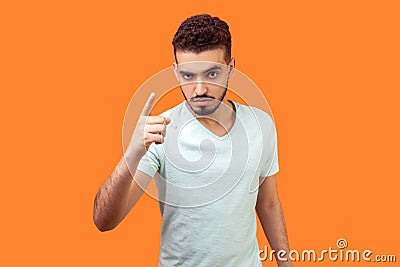 Be careful! Portrait of strict bossy brunette man warning you with raised finger gesture. indoor studio shot isolated on orange Stock Photo