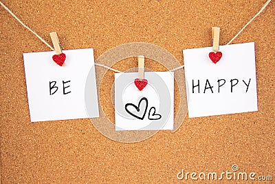 Be happy handwriting lettering on 3 white papers pinned with 2 big red heart pegs and one small red heart pegs on cork board Stock Photo