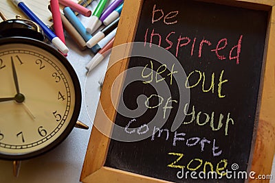 Be inspired get out of your comfort zone on phrase colorful handwritten on chalkboard, alarm clock Stock Photo