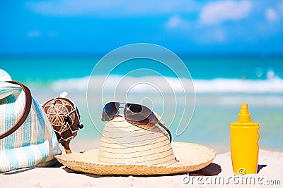Beach accessories on sand for summer vacation concept. Bag, maracas, straw hat with sunglasses and sunscreen lotion bottle. White Stock Photo