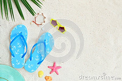 Top view of beach sand with coconut leaves, bracelet made of seashells, sunglasses, slippers, shells, starfish and straw hat. Stock Photo