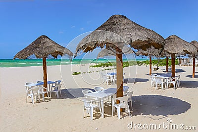 Beach bar - Tiki thatch umbrellas on sandy beach with white plastic chairs underneath and the turquioise sea and very blue sky on Stock Photo