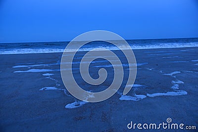 Tidal pools develop as night begins to fall along the sandy shoreline Stock Photo