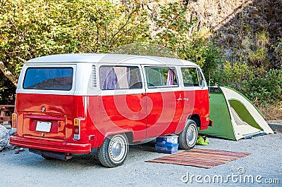 Beach campsite with red hippie minibus, green tent and rustic rug Stock Photo