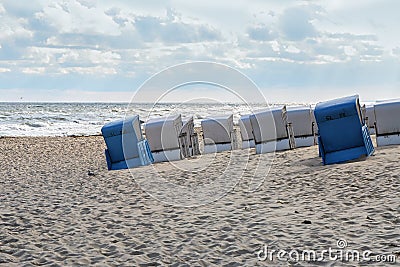 Beach chairs in blue and white from behind standing slanted on the sand in front of the waves on the shore of the Baltic Sea, Stock Photo