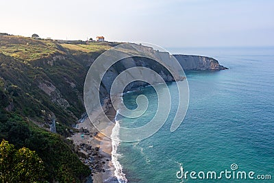 Beach and cliffs by the ocean at sunset. Small house on top of the hill at sunset time. Hidden beach at the botton of a cliff. Stock Photo