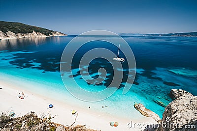 Beach leisure activity. Fteri bay, Kefalonia, Greece. White catamaran yacht in clear blue sea water. Tourists on sandy Stock Photo