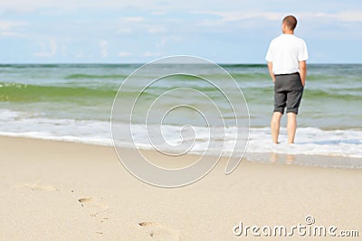 Beach man standing water back view shallow dof footprints Stock Photo