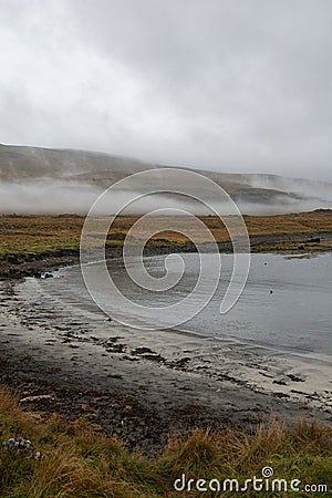 Beach by a peaceful lake, with lush green foliage surrounding the serene shoreline. Stock Photo