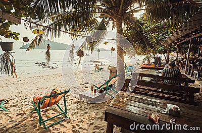 Beach restaurant with relaxing people, lounges on sand under palm trees and sea view. Happy holidays with ocean leisure Editorial Stock Photo