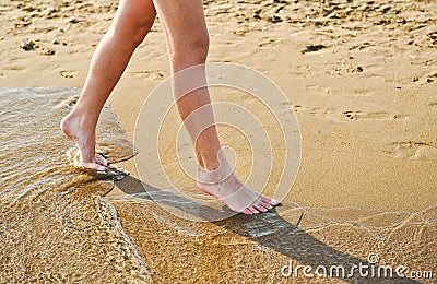 Beach travel - young girl walking on sand beach leaving footprints in the sand. Closeup detail of female feet and golden sand Stock Photo