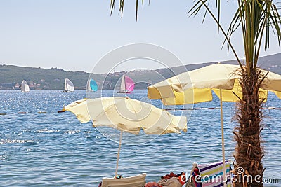 Beach vacation concepts. Beach umbrellas on coast, colorful sailboats on water. Montenegro Stock Photo