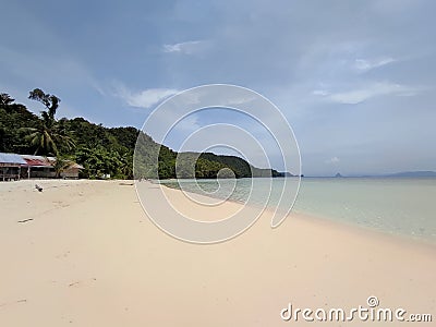 beachfront view on an island with white sand, clear blue sea water and small hills overgrown with green trees. Stock Photo