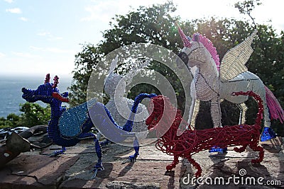 Beaded african artwork or curios placed on a rock wall at Chapmans Peak, Cape Town. The artwork are colourful dragons, unicorns Editorial Stock Photo