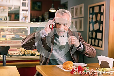 Beaming caring husband holding his red smartphone while calling wife Stock Photo