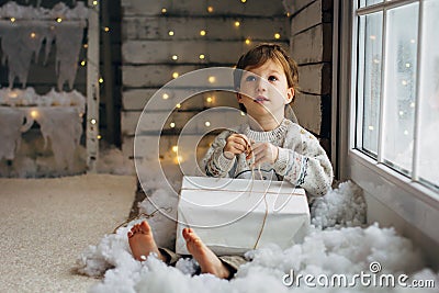 Beaming curlyhair boy opening his christmas gift. New Year lights background Stock Photo