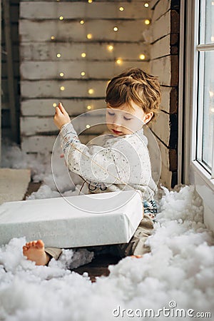 Beaming curlyhair boy opening his christmas gift. New Year lights background Stock Photo